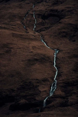 A long exposure captures a stream flowing down a hillside, showcasing blurred water motion and a dark, earthy-toned landscape.