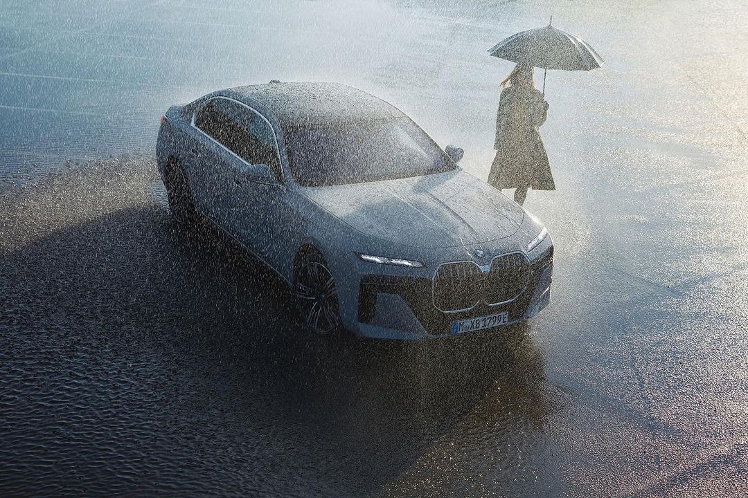 Grey BMW car in the rain with a person holding an umbrella in the background, creating a moody automotive scene.