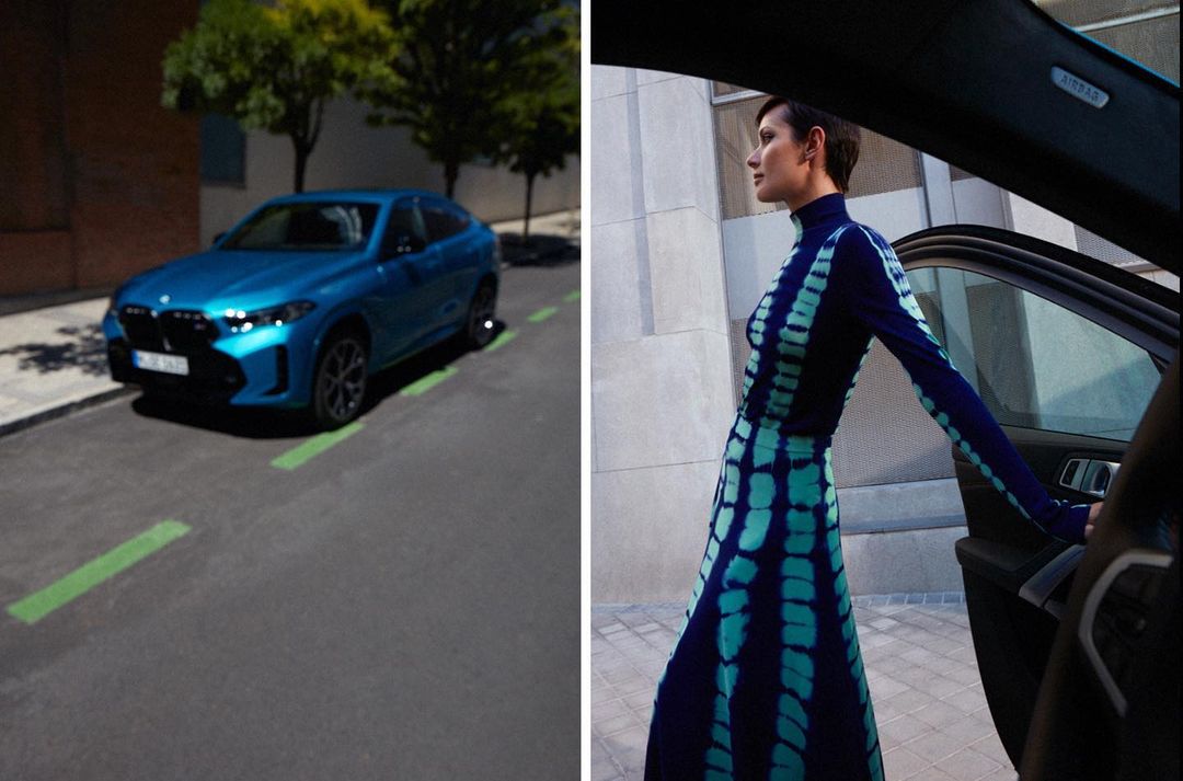 A woman in a patterned dress standing by a blue car on a city street, showcasing fashion and automotive elements.