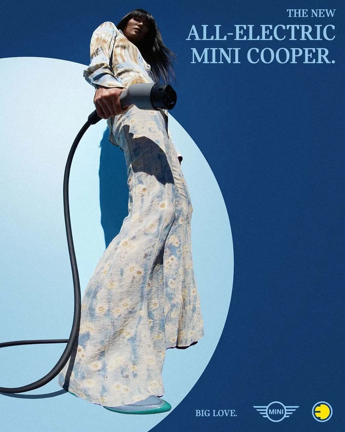 Low angle shot of a woman holding a large electric car charging cable against a blue background with text.