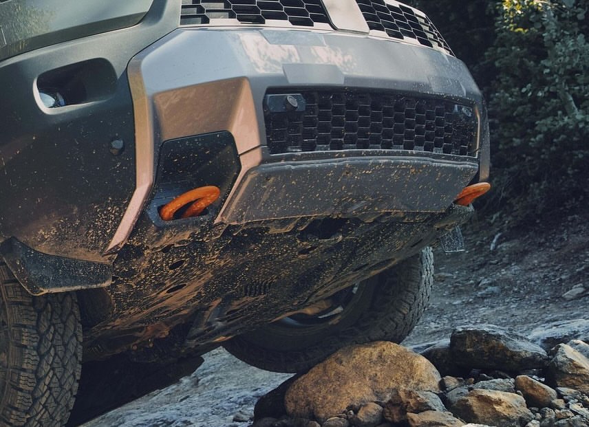 Close-up of the front of a gray SUV with orange tow hooks, captured from a low angle, emphasizing the vehicle's rugged design.