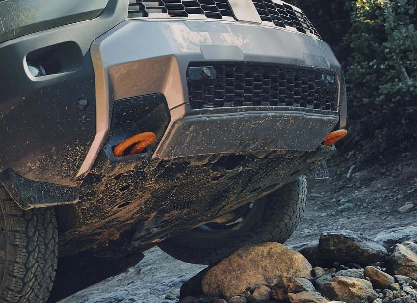 Close-up of the front of a gray SUV with orange tow hooks, captured from a low angle, emphasizing the vehicle's rugged design.