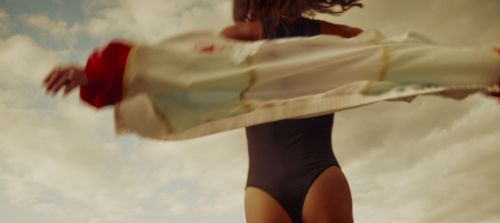 Woman in swimsuit turns and spins in sunlight, wearing a light coat against a background of a cloudy sky. Shot with a shallow depth of field.
