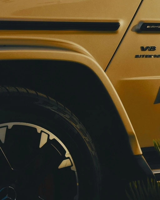 Close-up of a gold-colored Mercedes-AMG G63 SUV showing its black tire and V8 Biturbo badge. The vehicle is parked outdoors.