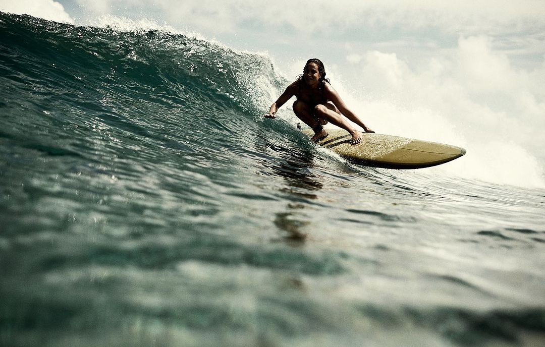 Woman in swimsuit riding a surfboard on a large ocean wave with cloudy sky, capturing the essence of water sports and summer adventure.