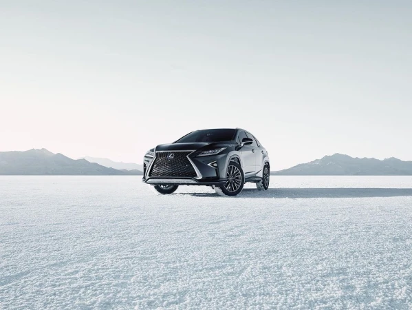 Dark grey Lexus SUV parked on a flat white surface with mountains in the distance under a bright sky, automotive product shot.
