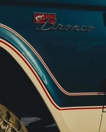 Close-up of a vintage blue and white Ford Bronco with the Bronco emblem, showcasing automotive design and classic vehicle aesthetics.