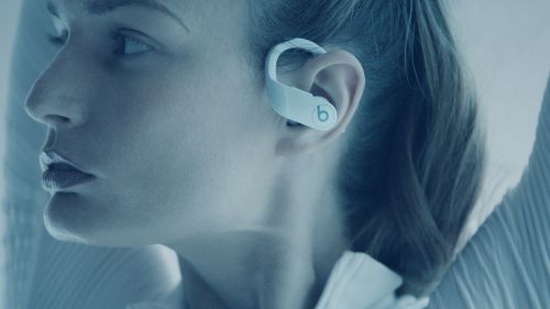 Close-up of a fair-skinned woman wearing Beats brand white wireless earbuds, showcasing a profile view in a soft, blue-toned light.