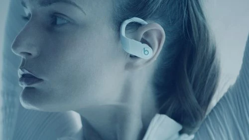 Close-up of a fair-skinned woman wearing Beats brand white wireless earbuds, showcasing a profile view in a soft, blue-toned light.