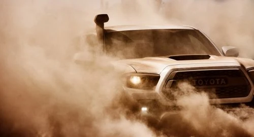 Off-road Toyota truck driving through the sand in a desert environment, leaving a cloud of dust, close-up perspective, natural lighting.
