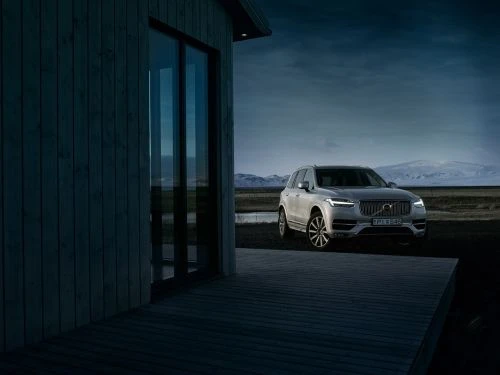 Silver Volvo SUV parked near a modern house at dusk with distant snow-capped mountains under a blue sky in a scenic outdoor setting.