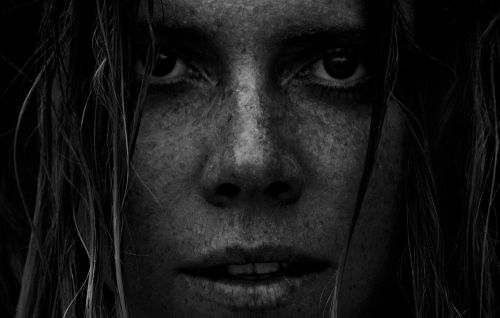 Extreme close-up monochrome portrait of a woman with freckles and dark wet hair framing her intense face.