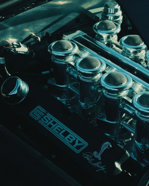 Close-up of a Shelby Cobra engine block showcasing the details of the air filters, chrome accents, and the iconic Cobra logo.