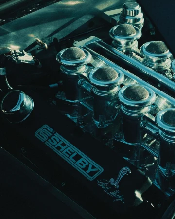 Close-up of a Shelby Cobra engine block showcasing the details of the air filters, chrome accents, and the iconic Cobra logo.