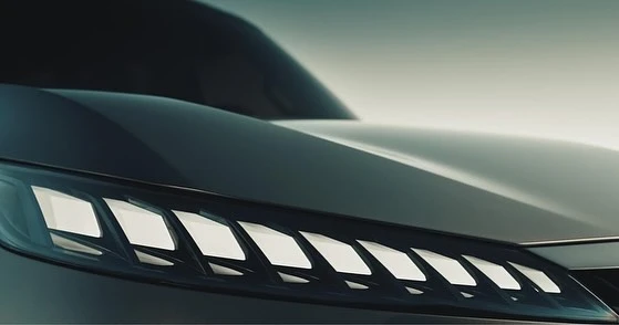 Close-up of the front of a gray car showcasing a modern headlight design with geometric shapes against a soft, neutral backdrop.