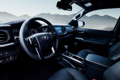 Interior view of a Toyota Tacoma truck featuring a black dashboard, steering wheel, and leather seats against a mountain backdrop.