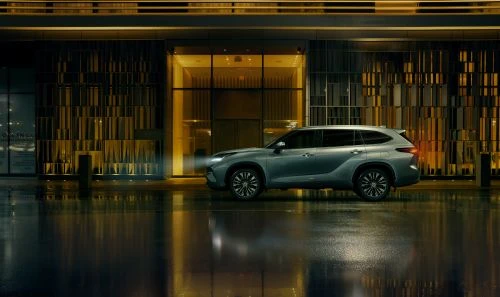 Silver SUV parked in front of a modern building at night, reflecting in the wet pavement after a rain, showcasing automotive design.