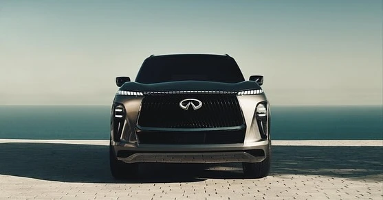 Frontal view of a dark grey Infiniti SUV with LED lighting details. A body of water extends across the horizon under a clear sky.