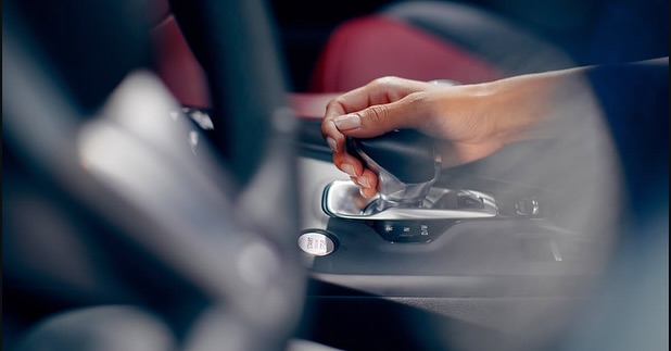 Close-up of a hand on the gear shift of a car, focusing on the center console and the 'start/stop' button.