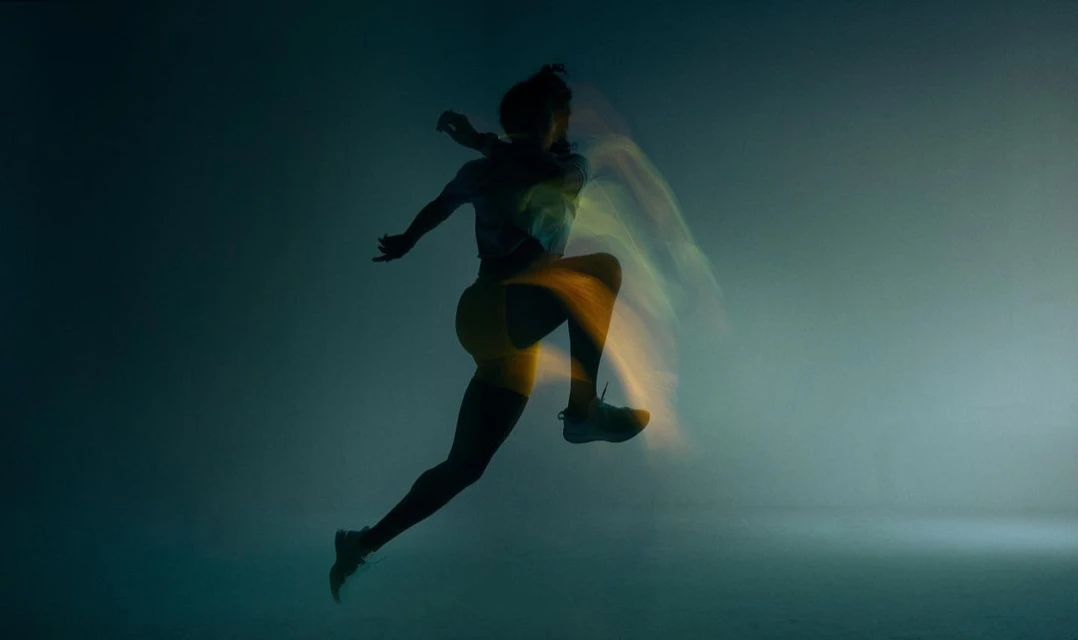A silhouette of a woman in motion mid-air, captured with a motion blur effect, set against a dark gradient background with light highlights.