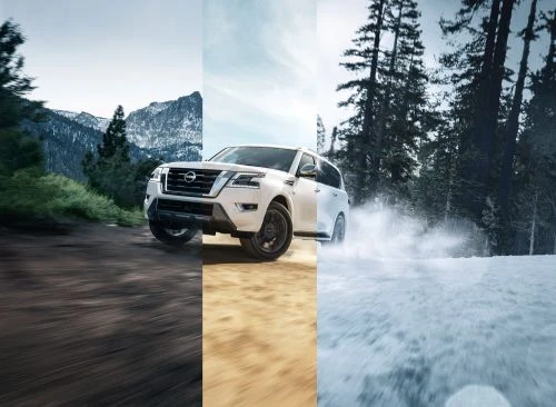 White SUV driving through various terrain: dirt, sand, and snow. Vehicle in motion with blurred background suggesting speed and adventure.