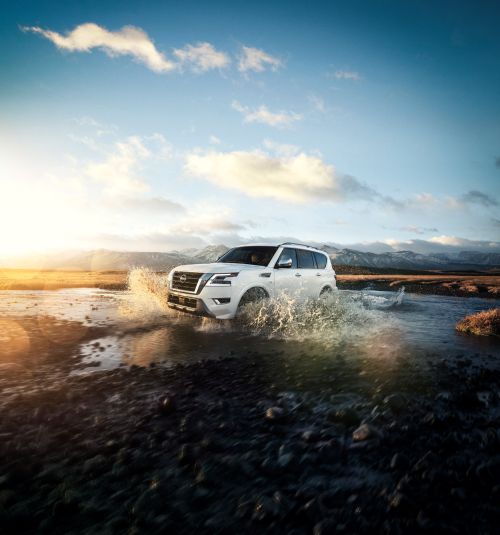 White SUV driving through water with a backdrop of mountains and a cloudy sky, showcasing automotive capability in a scenic environment.