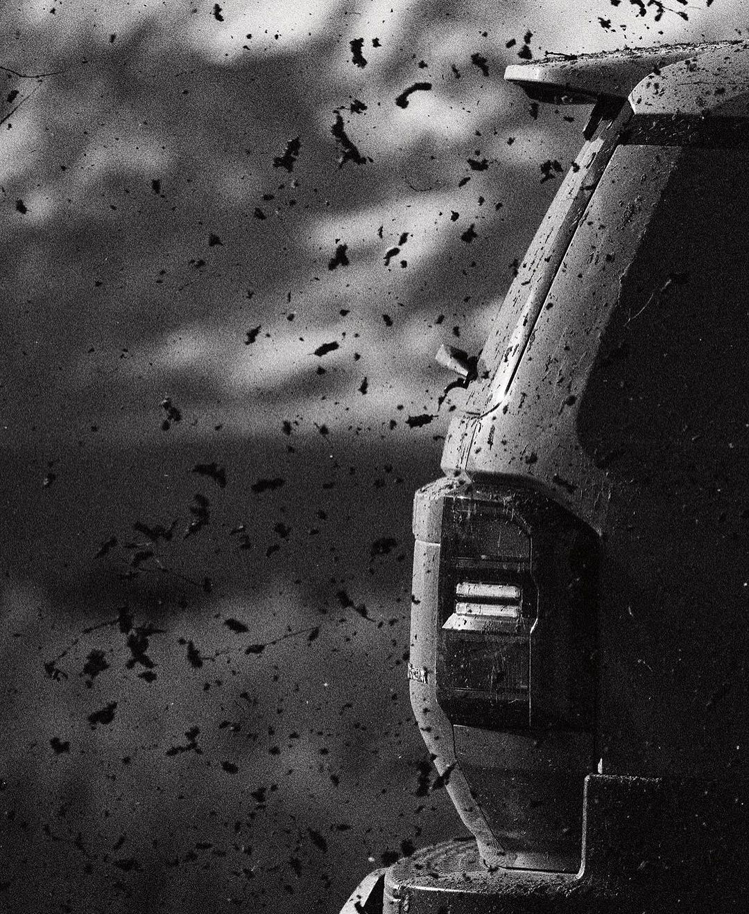 Monochrome shot of the rear of a truck covered in dirt, captured in a close-up, with a blurred background of dirt particles.