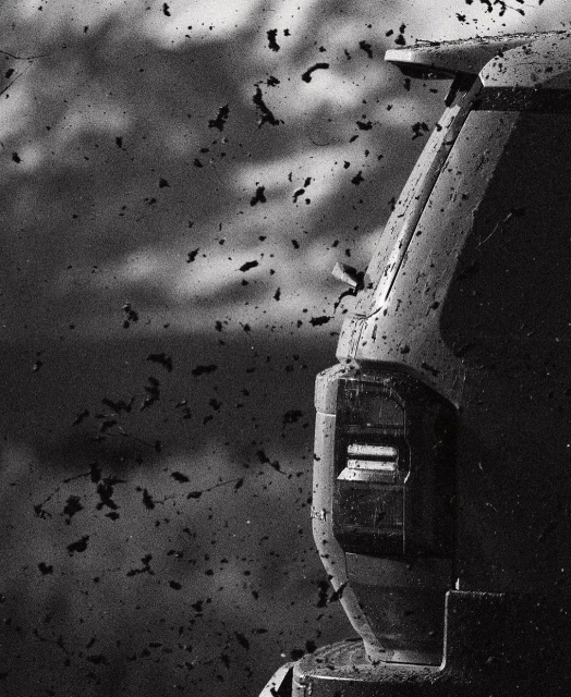 Monochrome shot of the rear of a truck covered in dirt, captured in a close-up, with a blurred background of dirt particles.