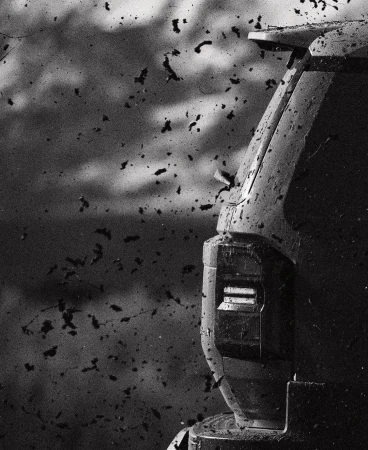 Monochrome shot of the rear of a truck covered in dirt, captured in a close-up, with a blurred background of dirt particles.