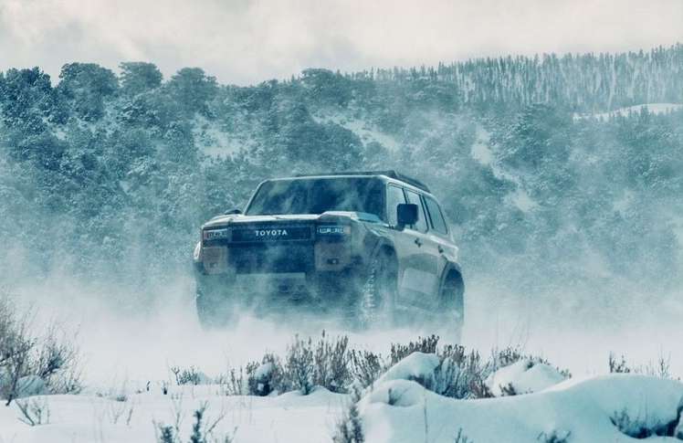 Toyota SUV driving on a snowy landscape with snow-covered mountain and forest in the background, in a winter setting and hazy daylight.