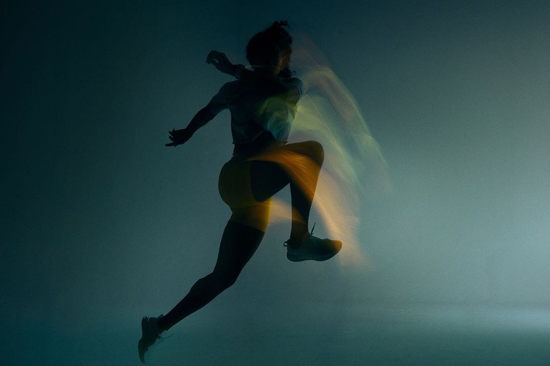 Silhouette of a runner mid leap captured with long exposure light trails against a dark moody background