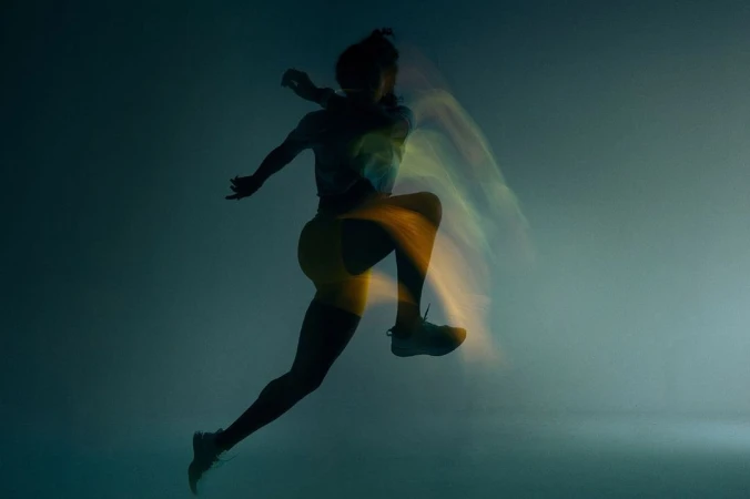 Silhouette of a runner mid leap captured with long exposure light trails against a dark moody background
