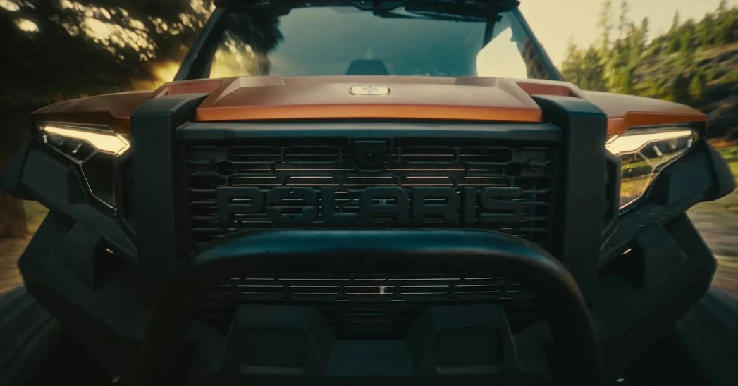 Front view of a Polaris off-road vehicle showcasing its grill, headlights, and rugged design against a blurred natural background.