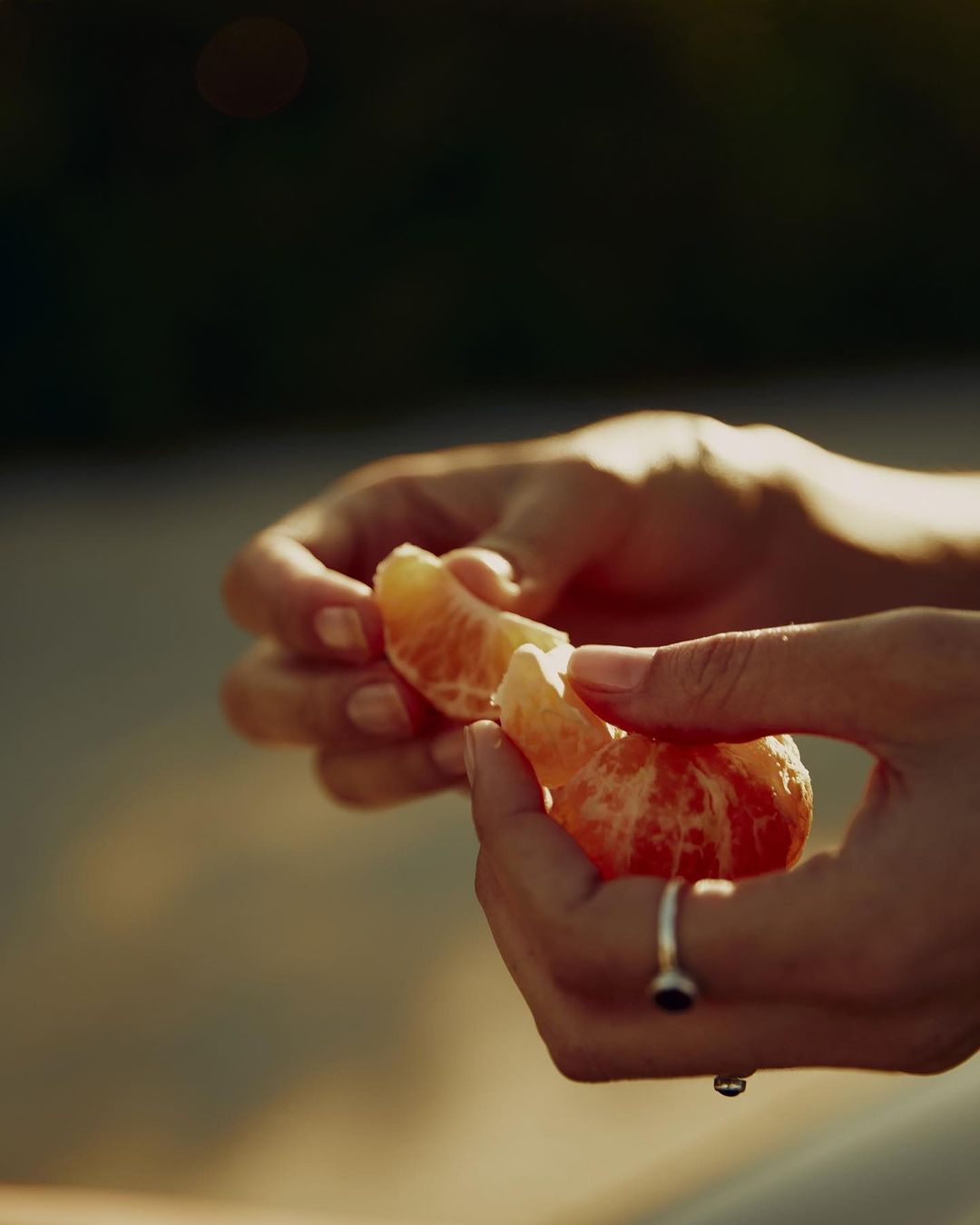 Close-up of hands peeling a juicy mandarin orange segment outside in warm light, highlighting its vibrant color and freshness.