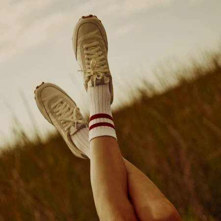 Legs lifted up in the air wearing white sneakers and striped socks against an outdoor blurry horizon