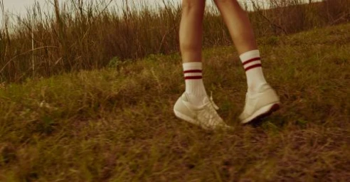 Close-up of legs walking through tall grass wearing white sneakers and ribbed socks with red stripes