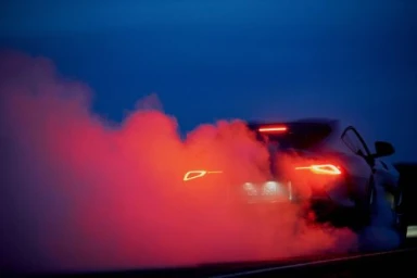 Rear view of a sports car surrounded by thick red and blue smoke from a burnout against a dark background
