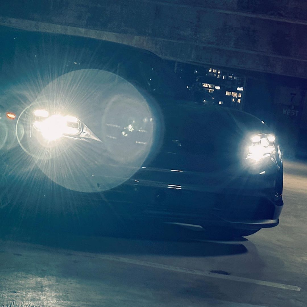 Sleek black car parked indoors at night, illuminated by bright headlights in an urban setting, highlighting its modern automotive design.