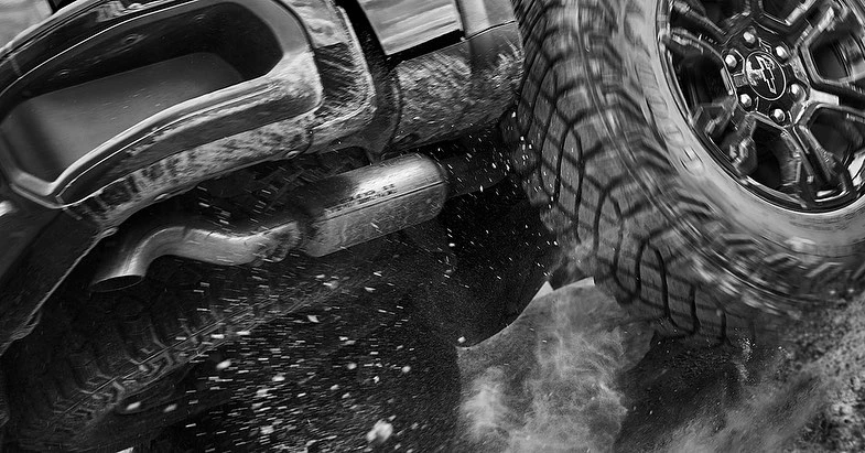Black and white shot of an off-road vehicle with its tire spinning, kicking up dust, capturing the power and ruggedness of automotive performance.