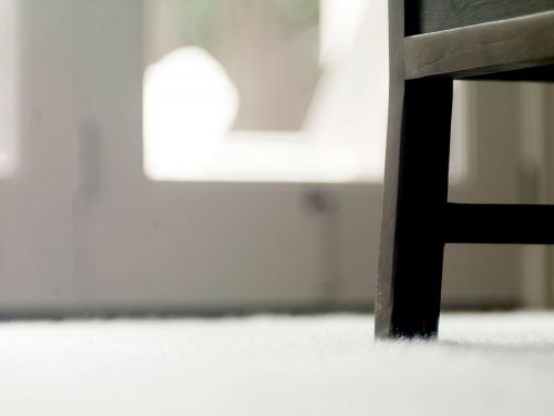 Close-up of a dark brown wooden chair leg resting on a white carpet, against a background of a white door and blurred interior.