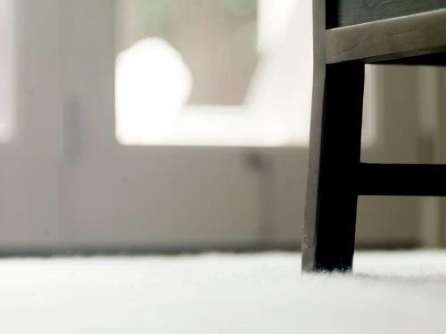 Close-up of a dark brown wooden chair leg resting on a white carpet, against a background of a white door and blurred interior.
