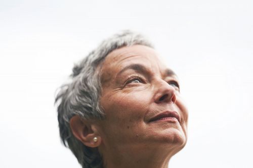 Close-up portrait of an elderly woman with short grey hair looking upward against a bright sky background