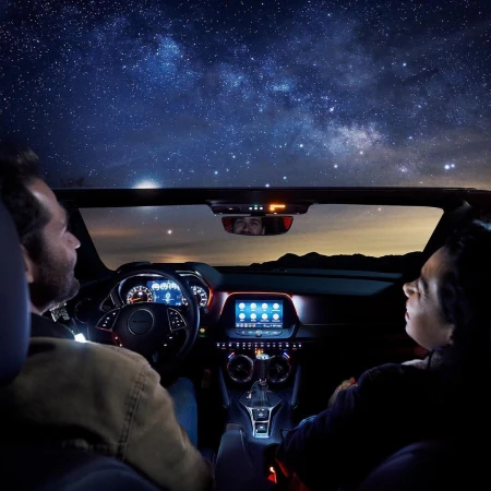 Two adult men in a convertible car interior looking up at a dark, starry night sky; car dashboard and controls are visible.