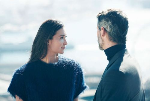 Portrait of a stylish couple outdoors during daytime, featuring a woman in a fuzzy blue sweater and a man in a black turtleneck and jacket.