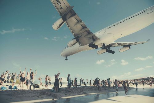 Airplane landing over Maho Beach with people watching at Saint Maarten, Caribbean. People standing on the beach are raising their hands to the plane.