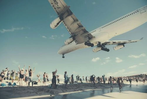 Airplane landing over Maho Beach with people watching at Saint Maarten, Caribbean. People standing on the beach are raising their hands to the plane.