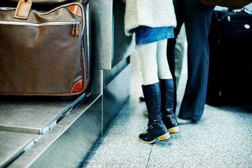 Travel scene featuring luggage on a conveyor belt, alongside people waiting at an airport, ready for their next destination.
