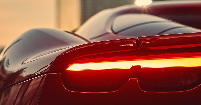 Close-up of the rear of a red sports car featuring a horizontal LED taillight and sleek spoiler. The car shows a modern design.