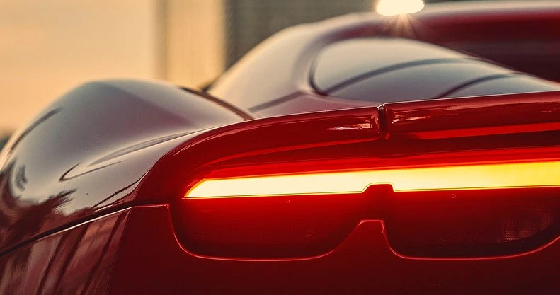 Close-up of the rear of a red sports car featuring a horizontal LED taillight and sleek spoiler. The car shows a modern design.