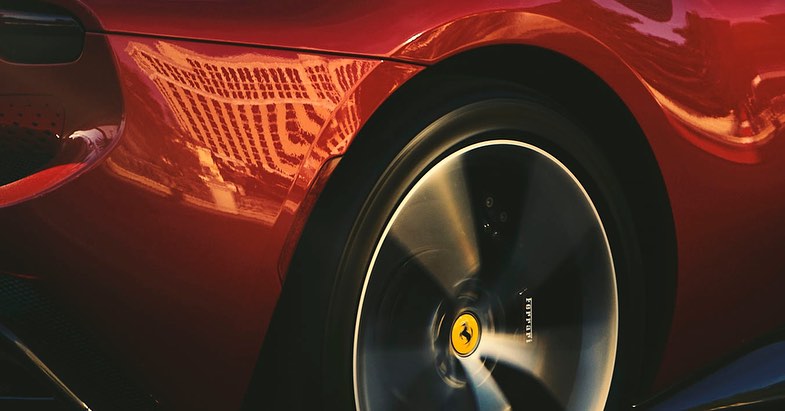 Close-up of a red Ferrari's rear wheel with black rim in motion and the car's body with a building reflection in the paint.